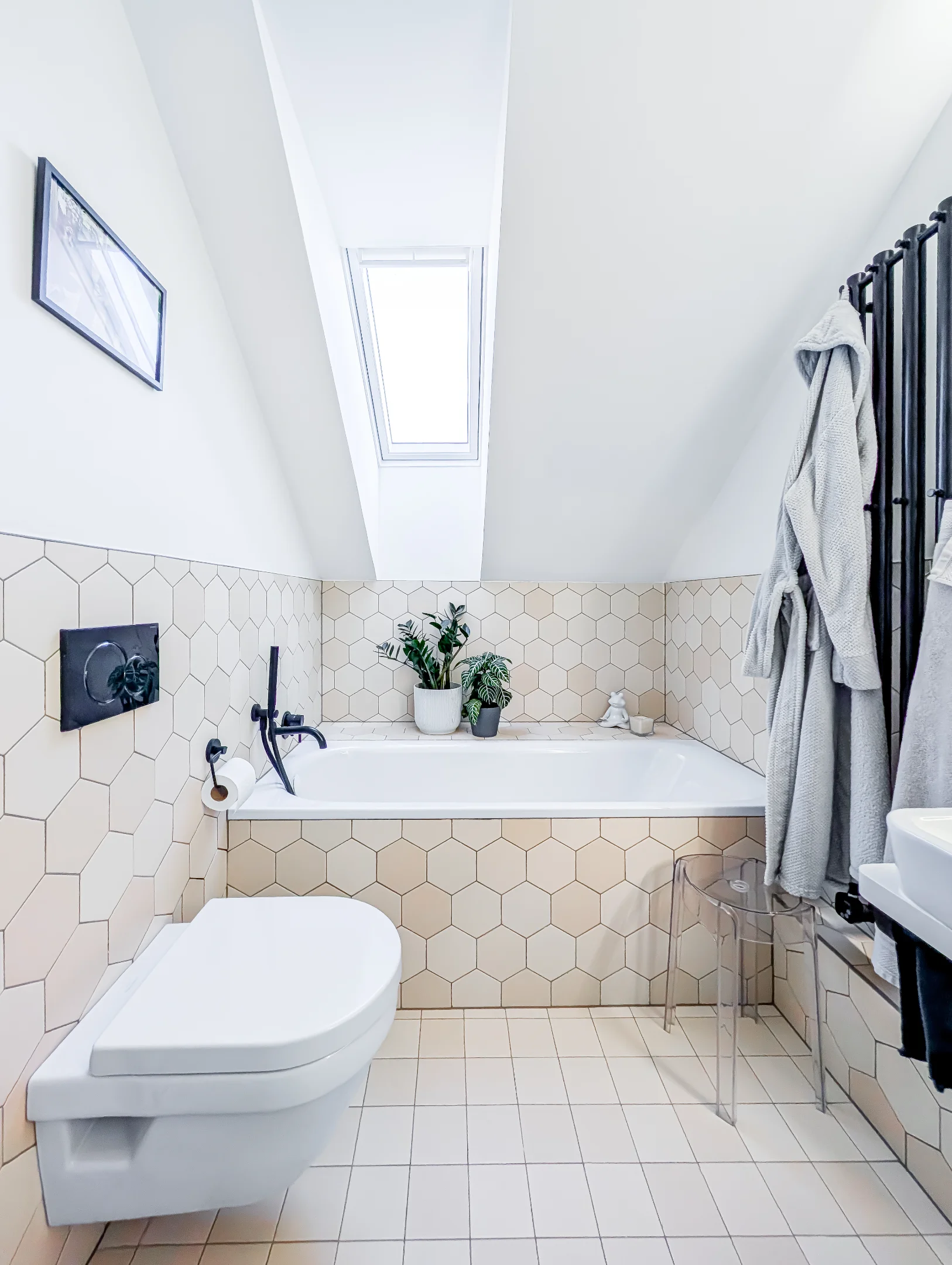 Bílá koupelna s vanou toaletou a střešním oknem.